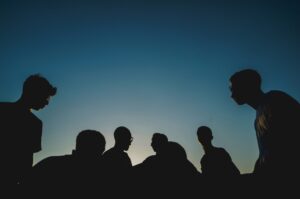Silhouettes of six people standing together against a clear blue sky at sunset.