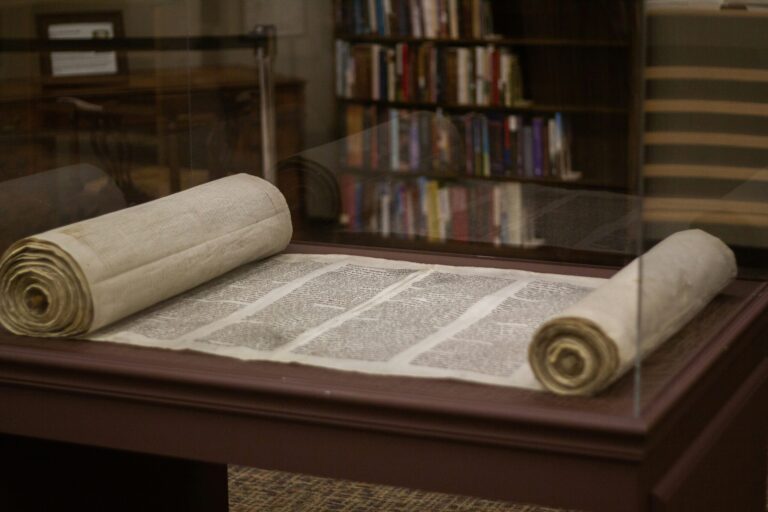 Ancient scroll displayed in a glass case, with bookshelves visible in the background.
