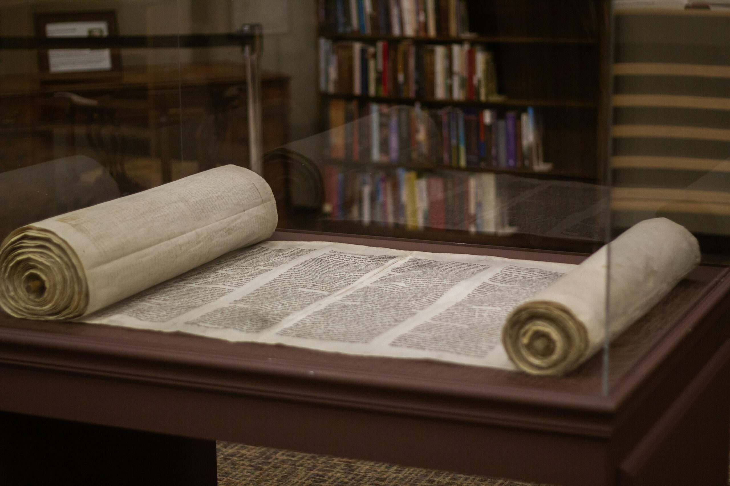 Ancient scroll displayed in a glass case, with bookshelves visible in the background.