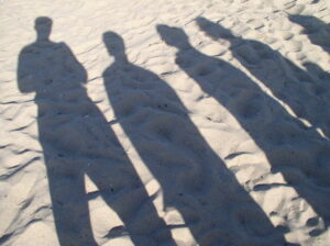 Shadows of four people standing on sandy ground in sunlight.