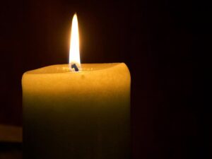 A close-up of a lit candle with a bright flame against a dark background.