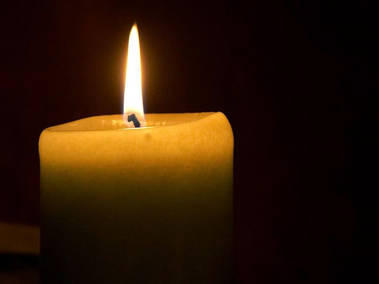 A close-up of a lit candle with a bright flame against a dark background.