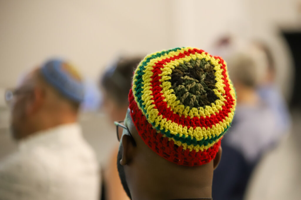 Person wearing a colorful crocheted cap, seen from behind, among a group of people in soft focus.