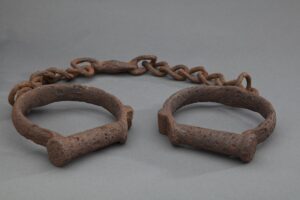 Rusty metal shackles connected by a chain, displayed on a plain gray background.