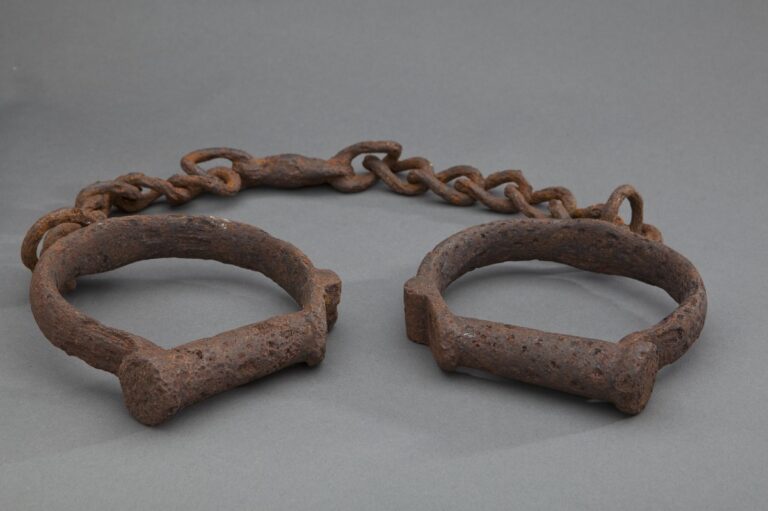 Rusty metal shackles connected by a chain, displayed on a plain gray background.