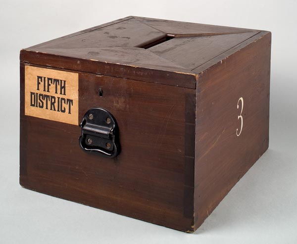 Wooden ballot box labeled Fifth District with a handle and the number 3 painted on the side.