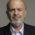 An older man with a bald head, gray beard, and mustache, wearing a suit jacket and light blue shirt.