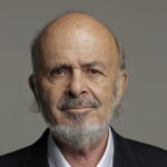 An older man with a bald head, gray beard, and mustache, wearing a suit jacket and light blue shirt.