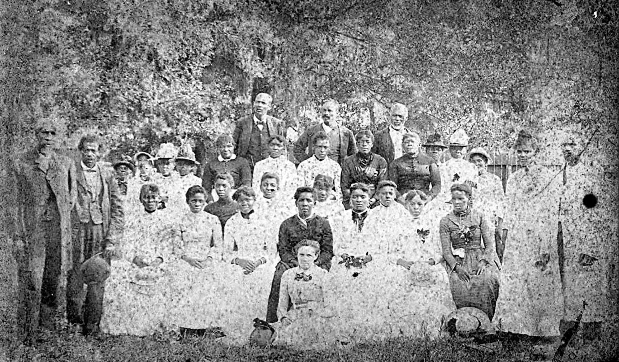 A vintage black-and-white photo of a large group of people posing outdoors in formal clothing.