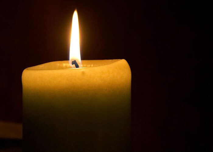 A close-up of a lit candle with a bright flame against a dark background.