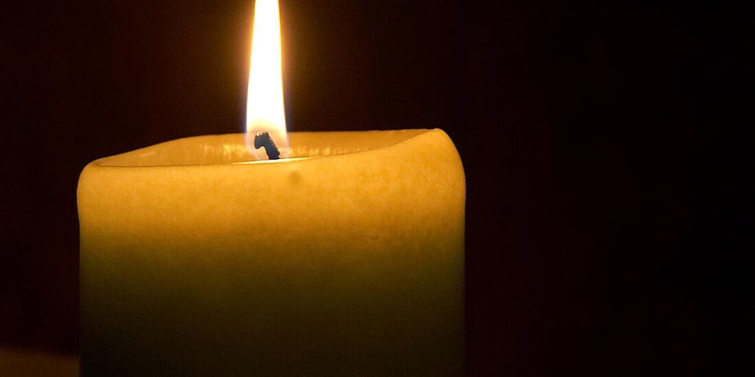 A close-up of a lit candle with a bright flame against a dark background.