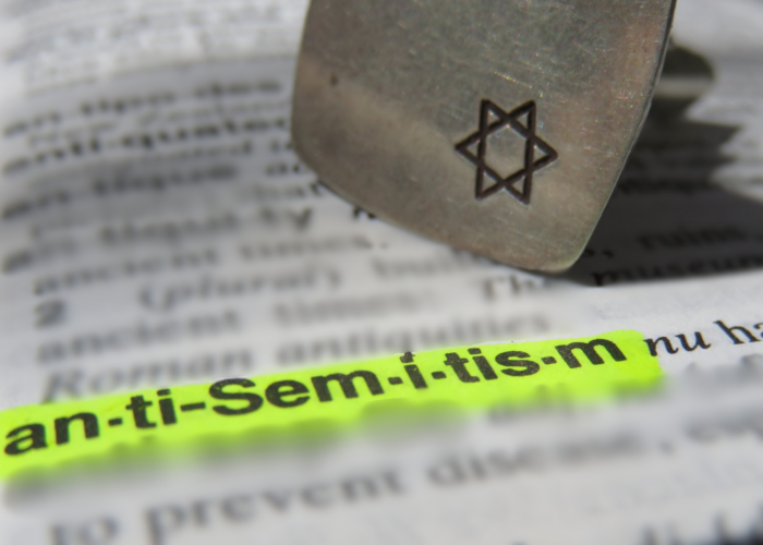 The word antisemitism is highlighted in a dictionary, next to a Star of David stamp.