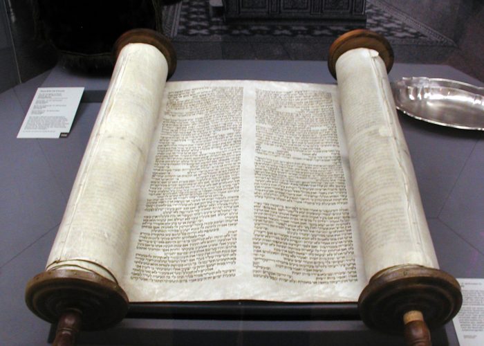 An open Torah scroll displayed on a stand with a decorative backdrop.