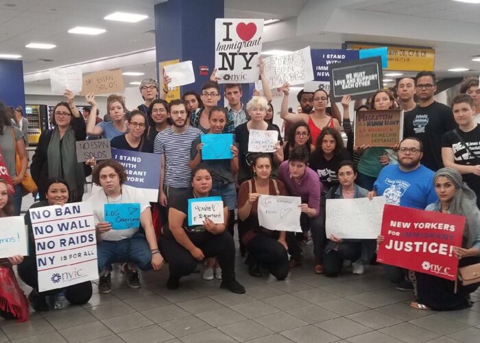 A group of diverse people holding signs supporting immigrant rights in a public indoor space.