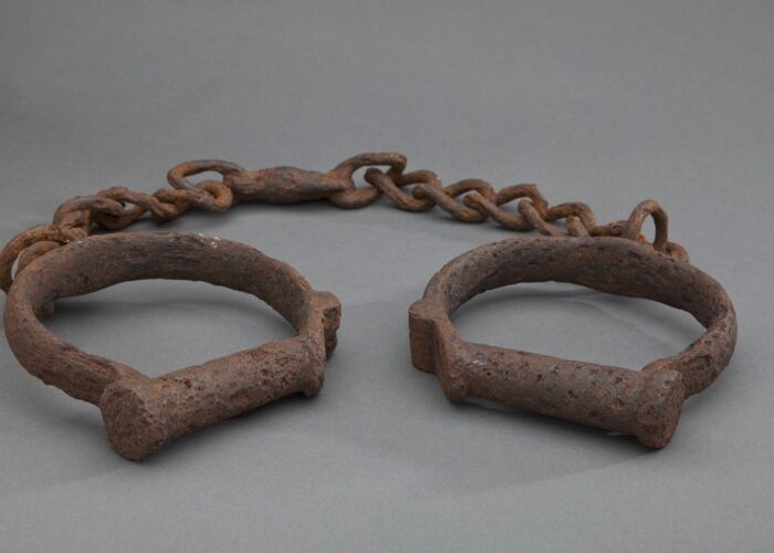 Rusty metal shackles connected by a chain, displayed on a plain gray background.