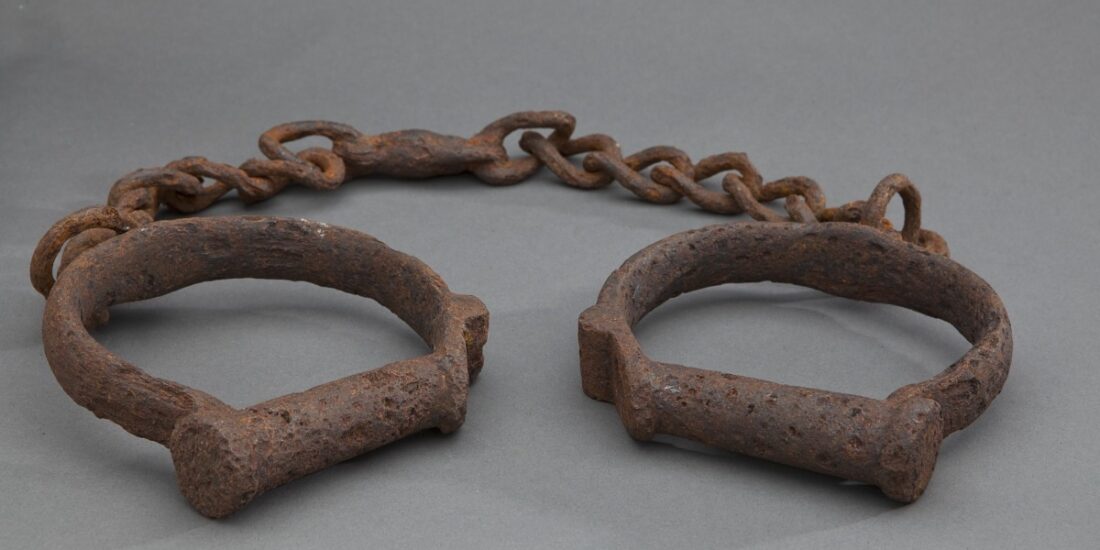 Rusty metal shackles connected by a chain, displayed on a plain gray background.