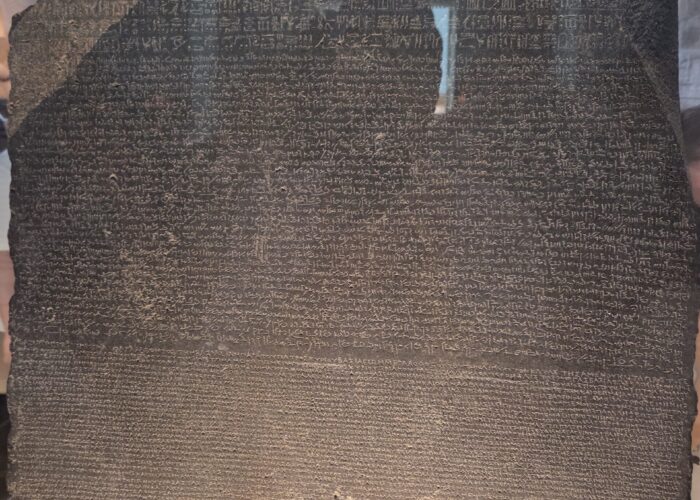 A large, dark stone slab inscribed with ancient text in three different scripts, displayed in a museum.