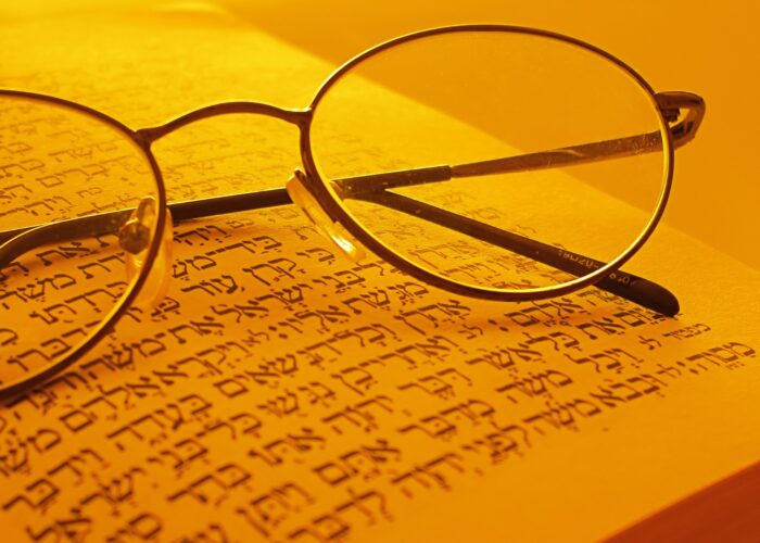 Round glasses resting on a Hebrew text page, illuminated by warm lighting.