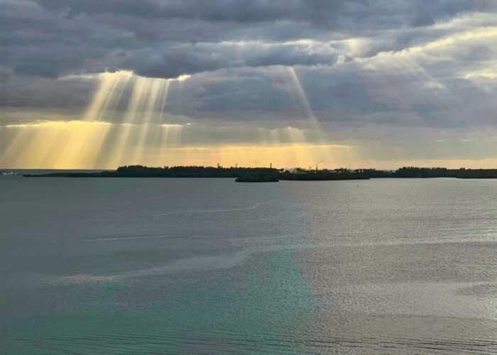 Sunbeams break through clouds over a calm body of water with distant islands on the horizon.