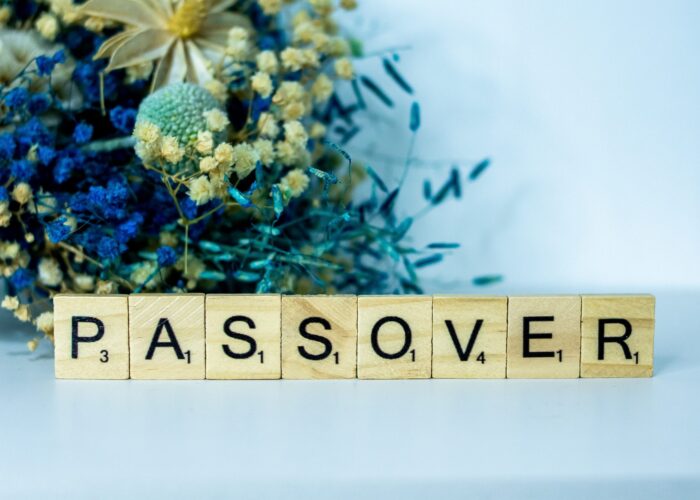 Scrabble tiles spelling Passover with a floral arrangement in the background.