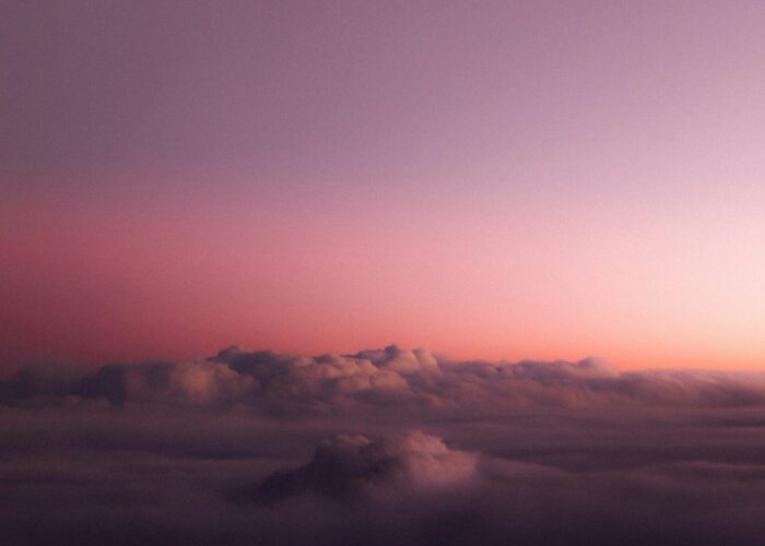 A serene view of a mountain peak emerging through soft clouds at sunset, with a purple and orange sky.