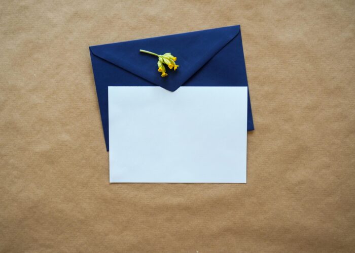 A white card with a blue envelope and a small yellow flower on a brown background.
