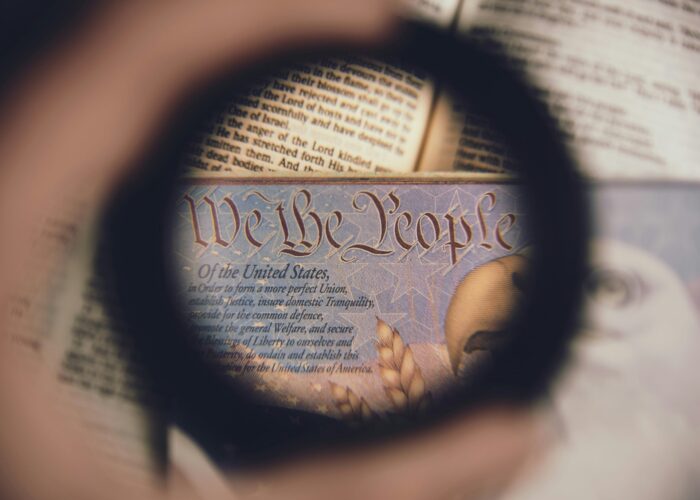 A magnifying glass focuses on the words We the People from the U.S. Constitution over an open book.