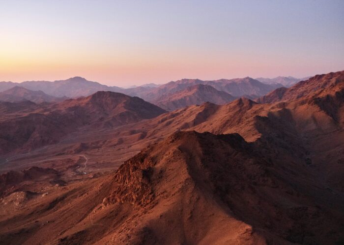 Mountain range at sunset with pink and purple hues in the sky and rugged peaks in the distance.