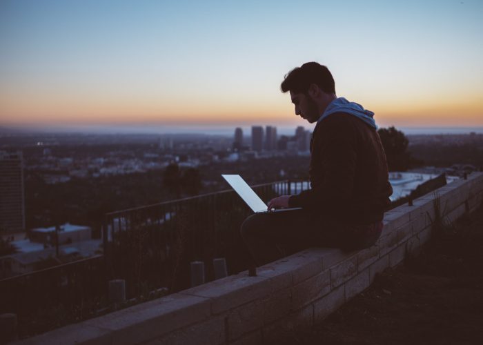 person sitting on balcony above city, working on laptop