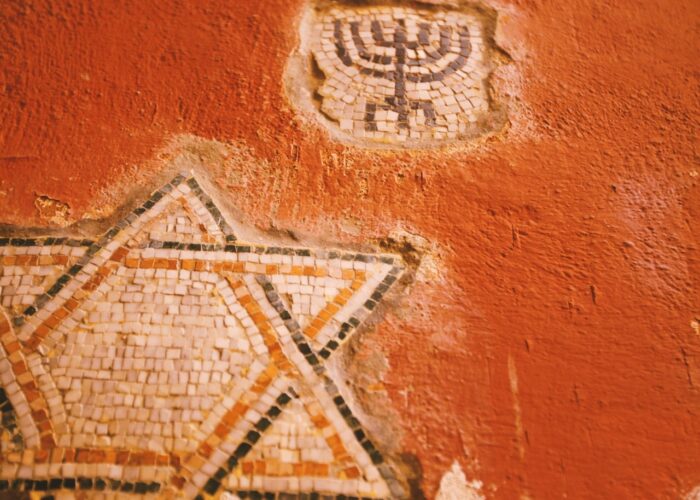 Mosaic Star of David and menorah on a textured, faded red wall.