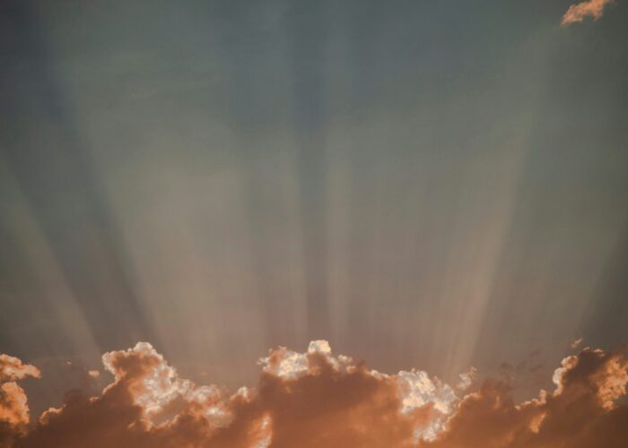 Golden clouds with sun rays streaming upward into a dusky sky.