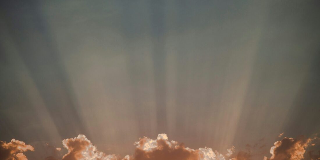 Golden clouds with sun rays streaming upward into a dusky sky.