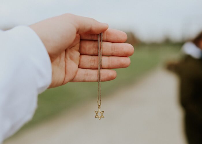 A hand holding a necklace with a Star of David pendant, outdoors.