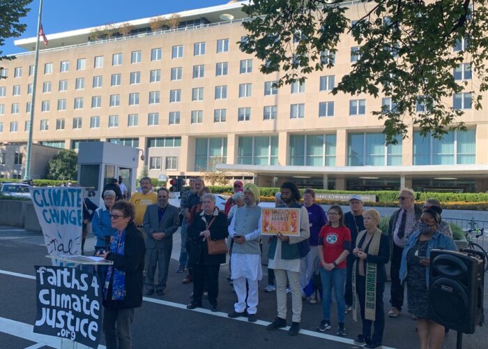 A group of people participate in a Faiths 4 Climate Justice rally outside a large building.