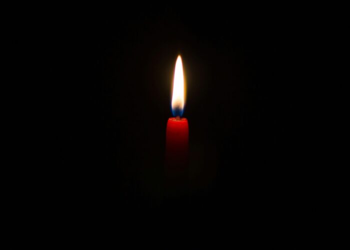 A single red candle burns in the darkness, with a bright, glowing flame.