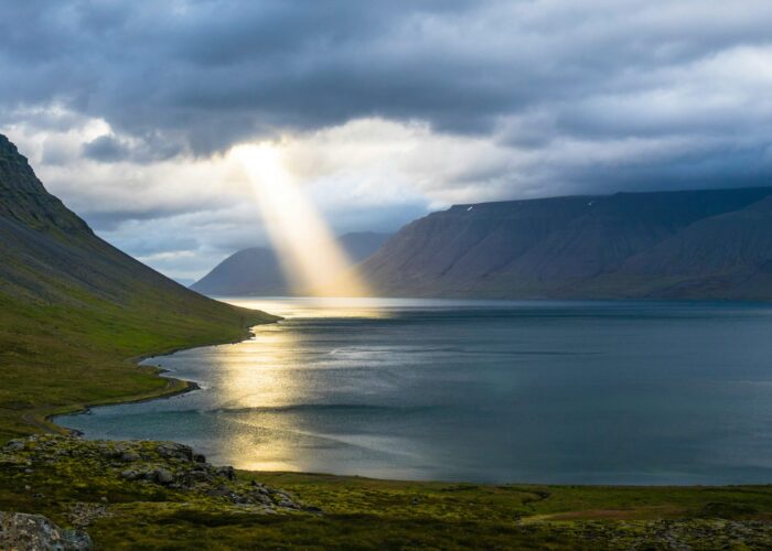 Sunbeam piercing through clouds over a serene fjord with mountains, creating a dramatic and peaceful scene.