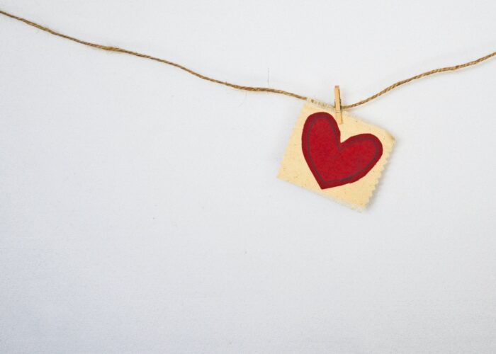 A red heart on a small paper is clipped to a string against a white background.