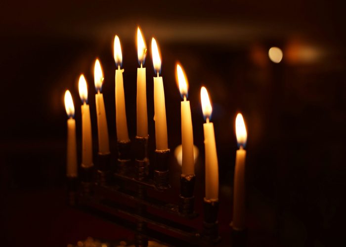 Nine lit candles on a menorah, glowing in a dark setting.