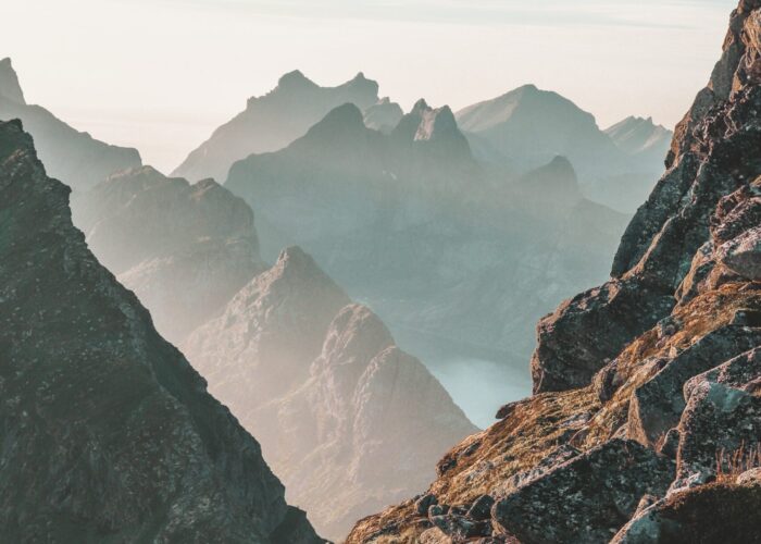 Mountain peaks with mist and rugged rocky terrain under a blue sky.