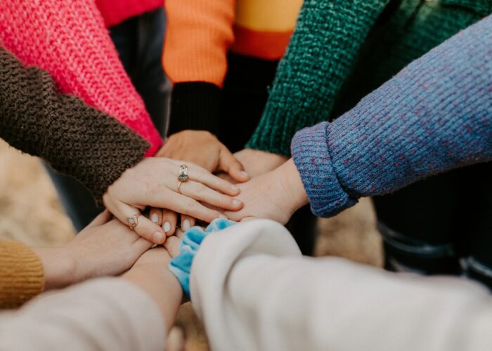 A group of people wearing colorful sweaters stack their hands together in a show of unity.