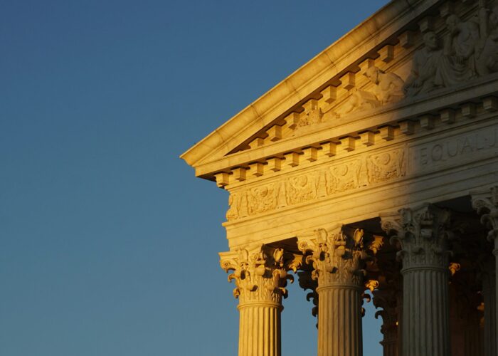 Sunlit columns and pediment of a classical building against a clear blue sky.
