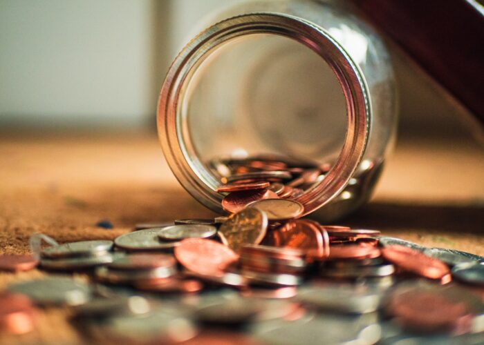 Coins spilling from a glass jar onto a table.