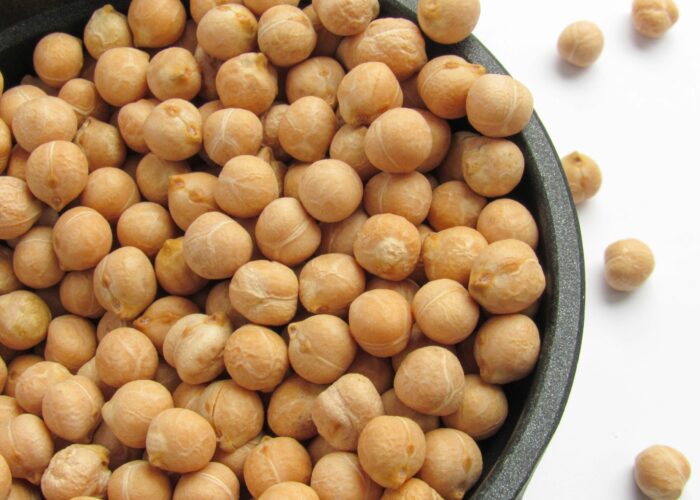 A black bowl filled with dry chickpeas, with a few chickpeas scattered on a white surface.