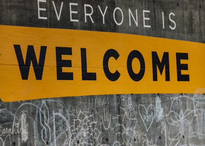 Chalk graffiti on a wall with the message Everyone is Welcome in bold yellow and white letters.