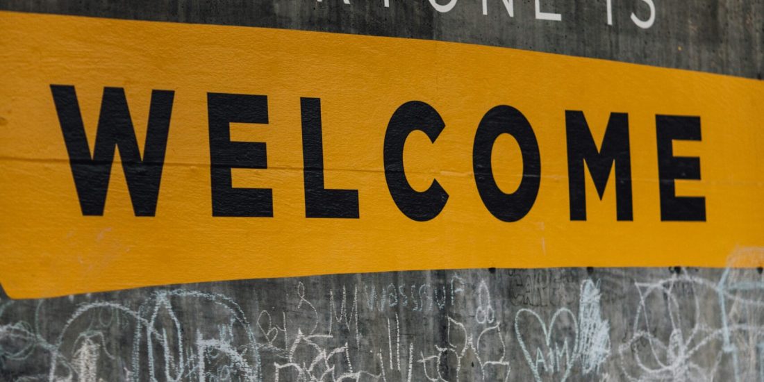 Chalk graffiti on a wall with the message Everyone is Welcome in bold yellow and white letters.