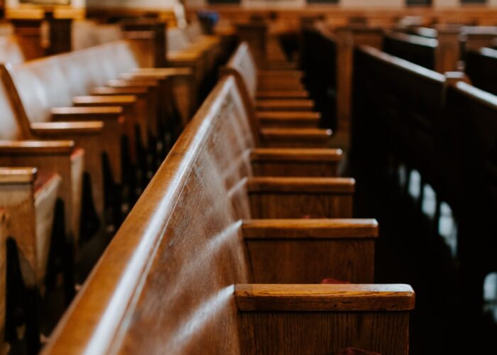 Empty wooden pews in a church with soft lighting illuminating the space.