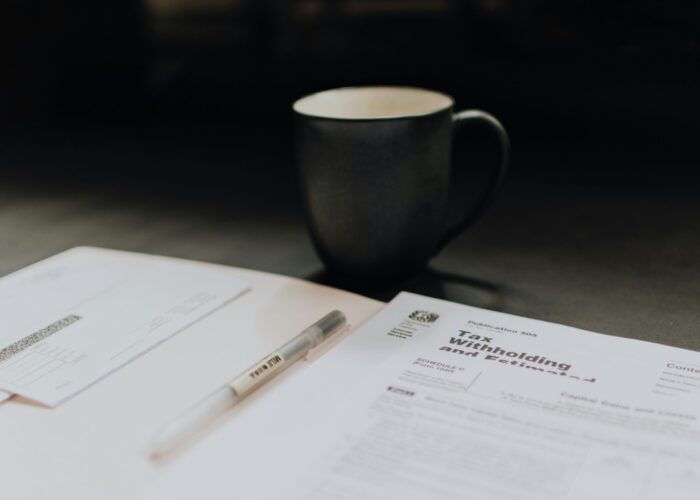 A coffee cup next to tax withholding forms and a pen on a table.