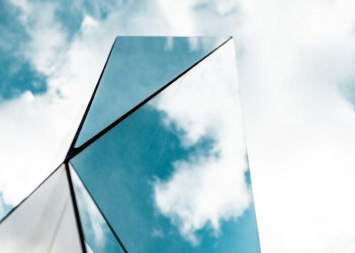 Tall reflective glass structure against a blue sky with scattered clouds.