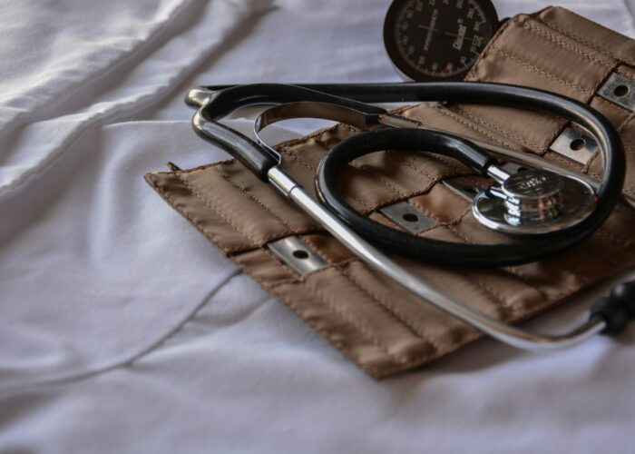 A stethoscope and a blood pressure cuff on a white surface, partially in a brown case.