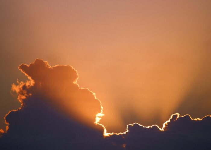 Sunset with dramatic clouds and golden-orange sky, creating radiant beams of light.